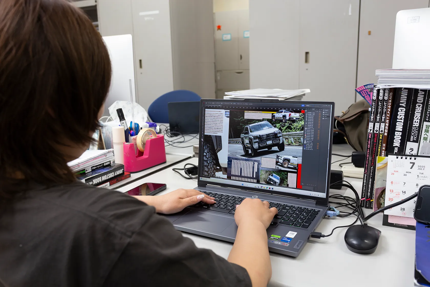 編集部のデスクで、パソコンを使って情報誌の編集作業を行っている様子。