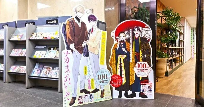 ぶんか社入口に展示された作品の等身大パネル。『ナカまであいして』などの人気BL作品が紹介されており、累計100万部突破やBLアワード2024第3位受賞といった実績が示されている。