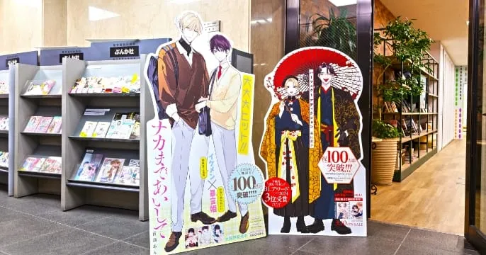 ぶんか社入口に展示された作品の等身大パネル。『ナカまであいして』などの人気BL作品が紹介されており、累計100万部突破やBLアワード2024第3位受賞といった実績が示されている。