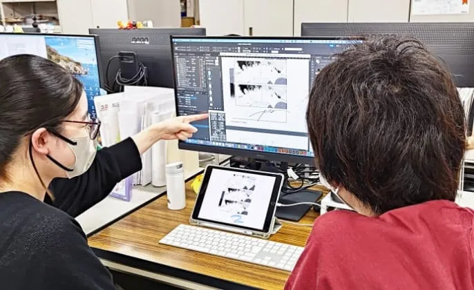 社内で、スタッフがモニターとタブレットを使って漫画原稿を確認しながら打ち合わせをしている様子。