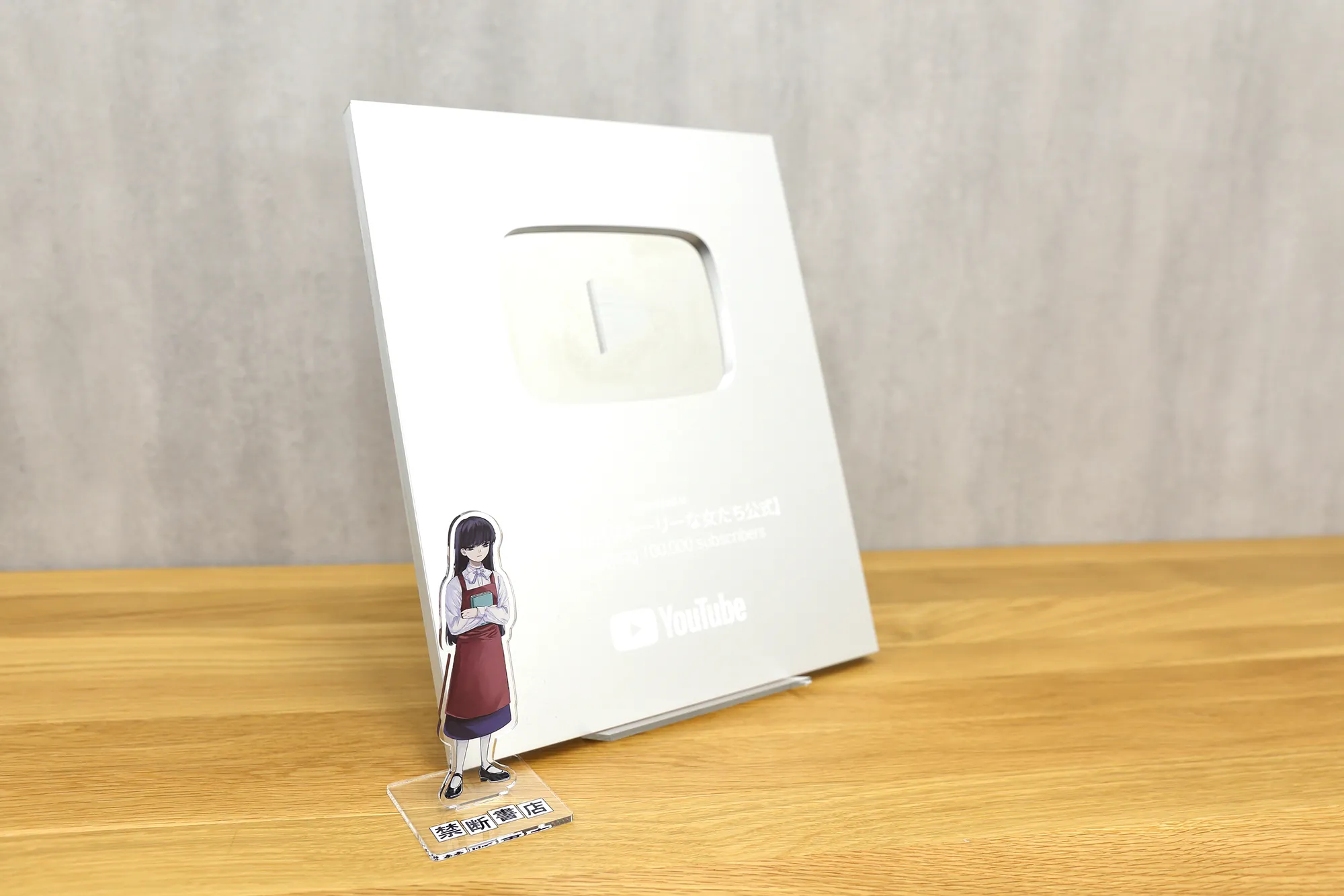 机の上に置かれたYouTubeのシルバークリエイターアワードとキャラクターのアクリルスタンド